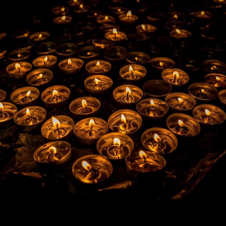 Viele kleine brennende Kerzen im Dunkeln, deren Licht ein warmes, stilles Muster bildet.